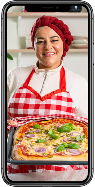 En bild som visar en mobil med Zeina Mourtada. Hon håller i en pizza som hon har lagat i köket.